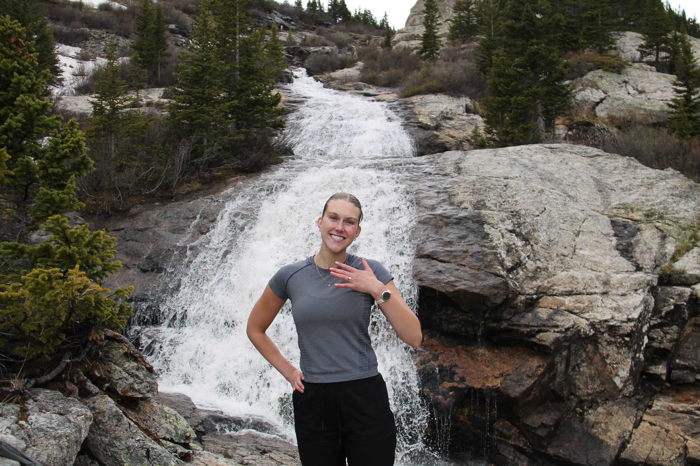 Tysen and Alyssa embracing on the rocks beneath a cascading Colorado waterfall