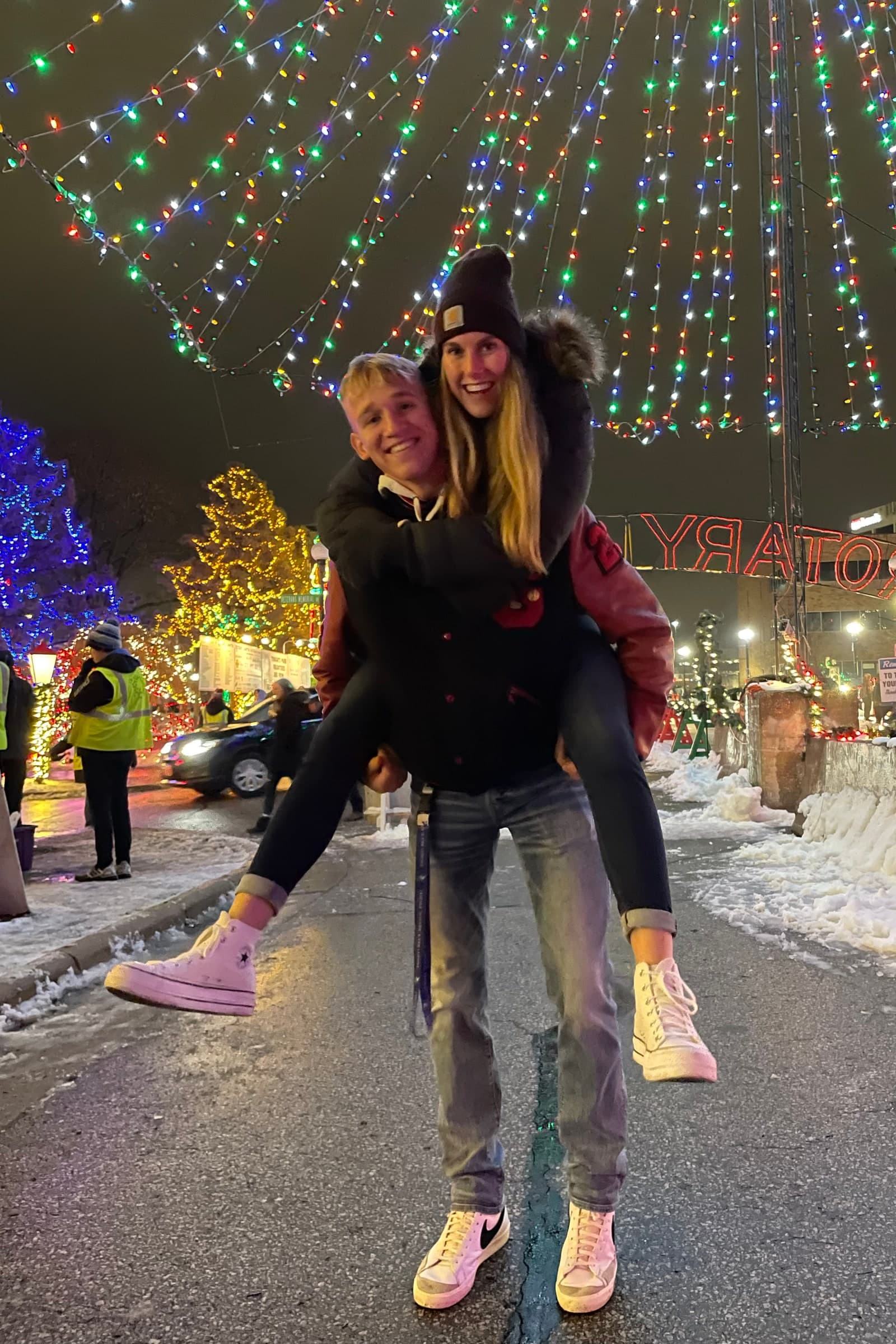 Tysen carrying Alyssa beneath Christmas lights in their college years