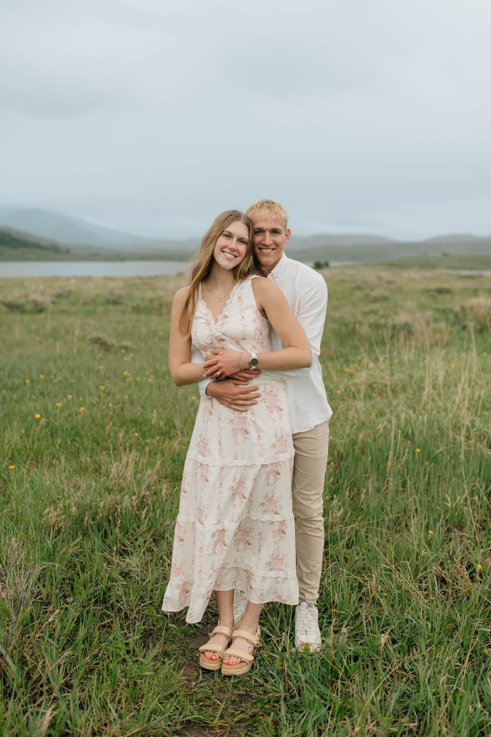 Alyssa and Tysen embracing in a green meadow with mountains behind them